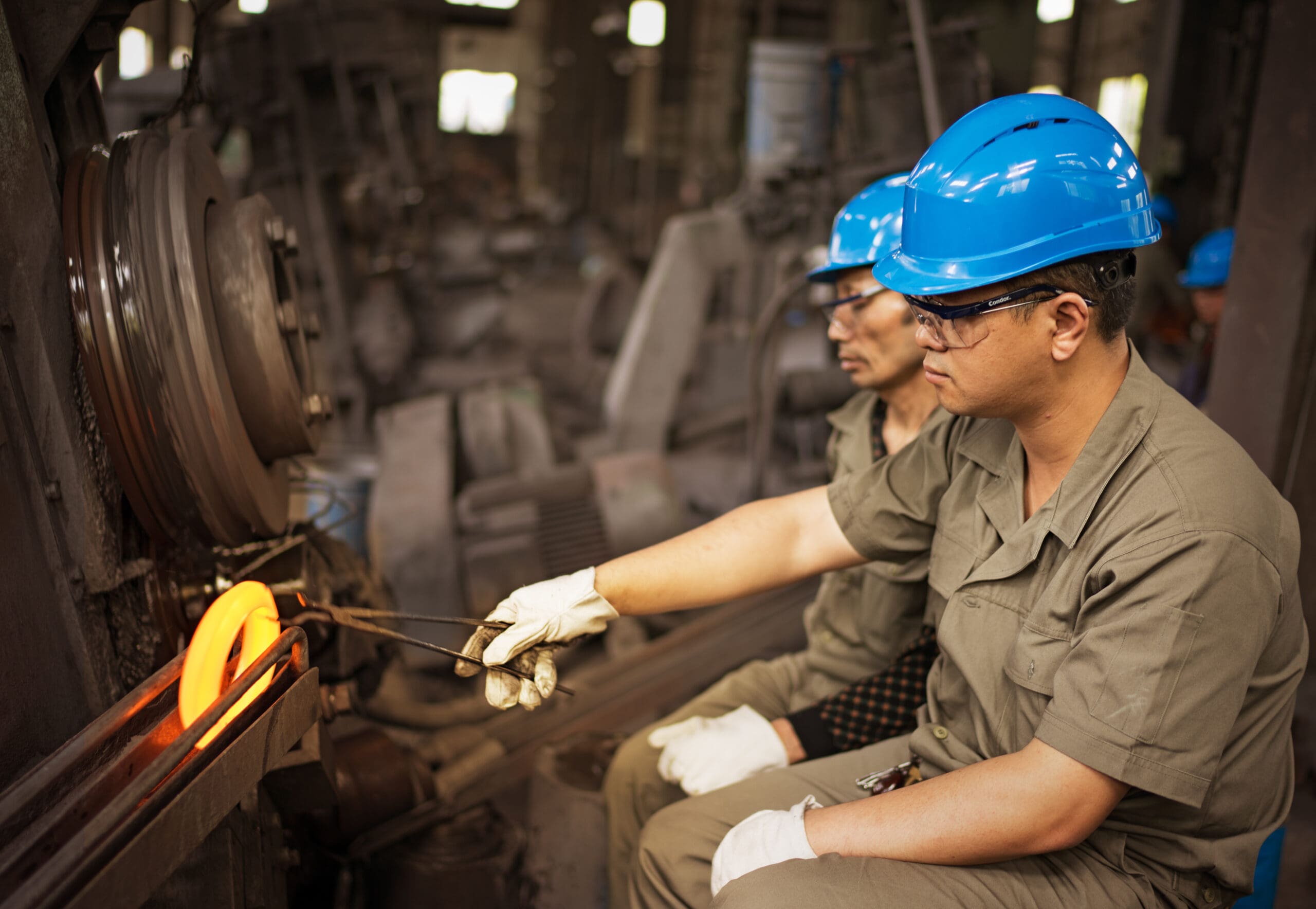 A mill operator picking up a glowing hot ring rolled forging.