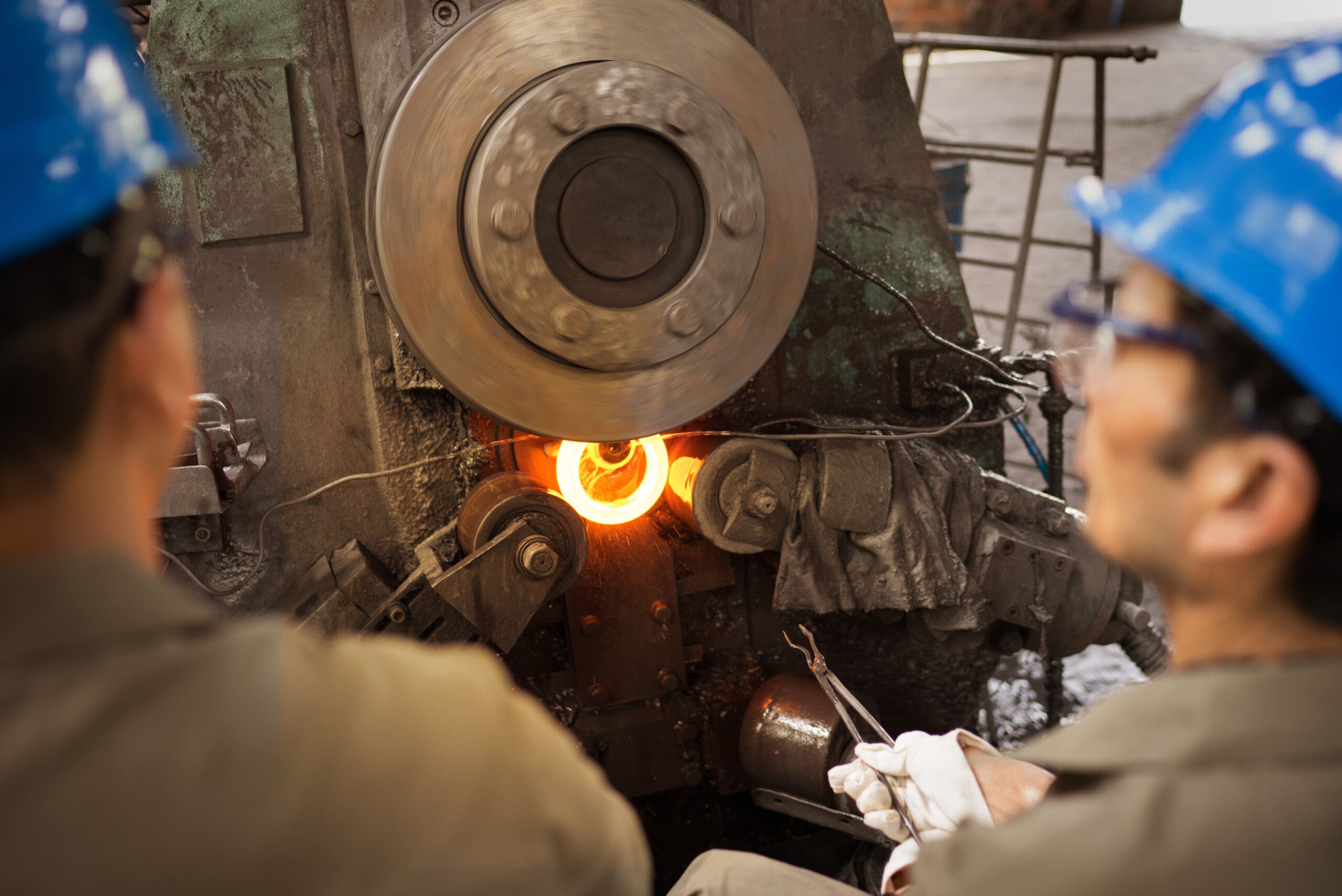 Vertical ring rolling mill operated by two workers, producing glowing ring rolled forging.